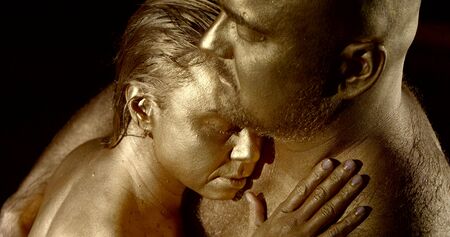 couple with gold paint on skin hugs in water slow motionの写真素材