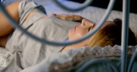 Close-up of a slender young woman in the bedroom on the bed, she lies in a short gray pajamas at the...