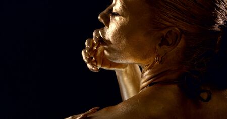 attractive golden painted lady runs fingers with manicure on long nails along lips and cheeks slow...