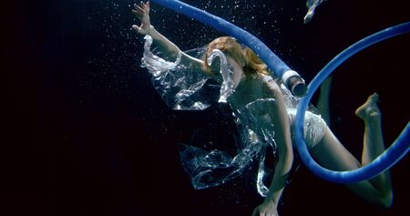 a slender girl is in a dark Studio under water, on her underwear. There are bubbles and debris...