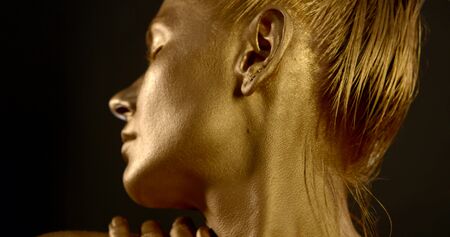 closeup face of woman with golden greasepaint on skin and hair, moving hands