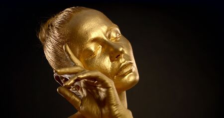 sensual woman covered gold is posing in studio in dark background