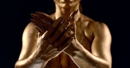woman painted golden shiny dye is stroking her palms, closeup view