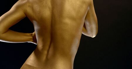 close-up of a womans back with Golden glowing skin and lingerie on a black background. the girl...