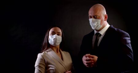 portrait of a couple in business clothes on a black background. they put disposable masks on their faces, look at each other, talk, gesture and disagreeの写真素材