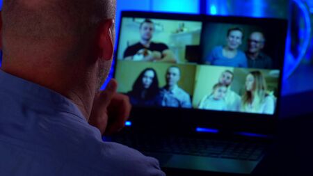 Close-up portrait of a bald middle-aged man, seen from the back, he is communicating on a laptop via...