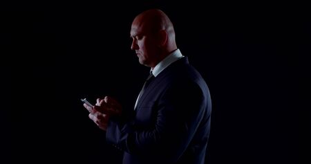 middle aged serious businessman is using smartphone, typing messages, swiping screenの写真素材