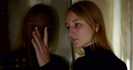thoughtful woman in black touches mirror in room slow motionの写真素材