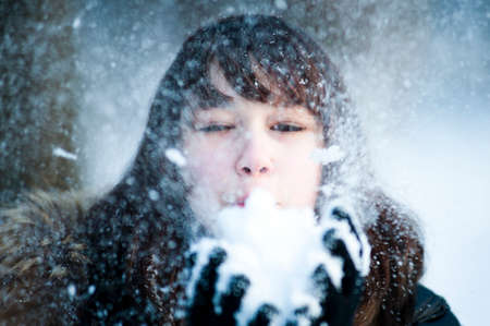 Close-up Portrait of a young beautiful happy woman. A model poses outside blowing snowflakes towards the cameraの写真素材