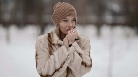 woman is feeling cold outdoors at winter day, warming palms by breath walking in park