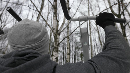 workout of adult man at winter, athlete is using free gym equipment in open sport area in park