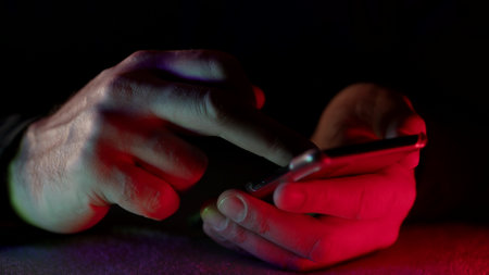 man is typing message on cell phone in darkness, closeup of hands with modern gadgetの写真素材