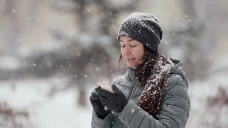 portrait of woman with smartphone outdoors at winter day, snowfall
