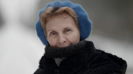 Portrait of an elderly woman in winter clothes, standing outdoors in a park in winter, looking at...