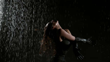 sensual lady is dancing under rain flows in darkness, waving long dark hairの写真素材