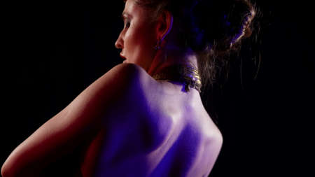 sexual half-naked dancer is moving slowly in darkness, rear view on naked shoulders