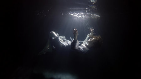 silhouette of sinking woman underwater, floating and diving under surface of dark poolの写真素材