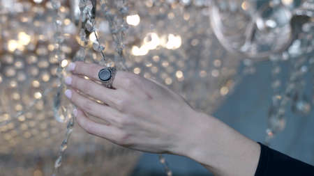 woman is stroking shiny crystal chandelier, closeup of hand, romantic and dramaticの写真素材
