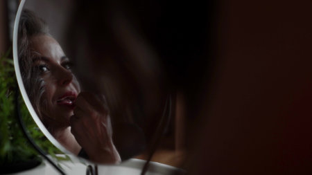 sexy woman is applying red lipstick, looking at mirror in her room, femininity and sensualityの写真素材