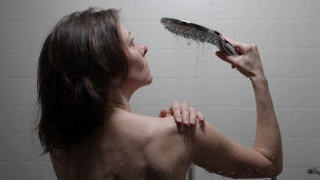young woman in shower, lady is pouring her naked body by water, rear viewの写真素材