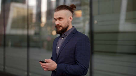 nervous and depressed man is checking news in internet by smartphone, outdoors of office buildingの写真素材