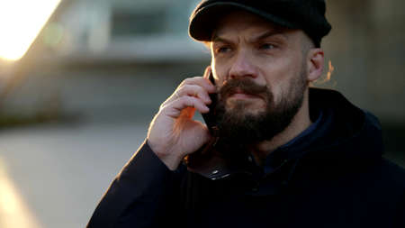 man with beard and moustache is chatting by cell phone in city street, portrait