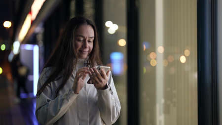 charming female dweller of megapolis is using smartphone outdoors in night, sending message