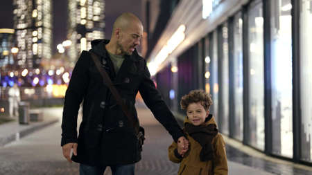 happy father and his little son are walking together in center of megapolis in eveningの写真素材