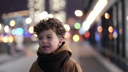 lost little child is walking on street in night, curly boy is going alone in city districtの写真素材