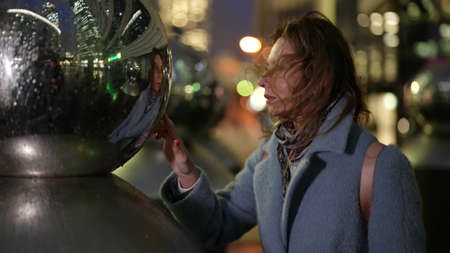 adult woman is viewing her reflection in modern art sculpture on city streetの写真素材