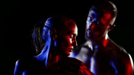 amazing sensual shot of two lovers in darkness, man and woman are covered by shiny golden dyeの写真素材