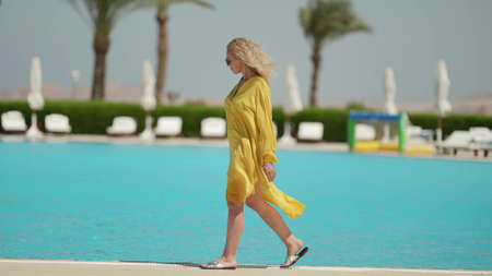rest in luxury hotel, woman is strolling along open pool in sunny dayの写真素材