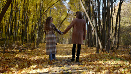 romantic walk in autumn forest, man and woman are holding hands, rear viewの写真素材