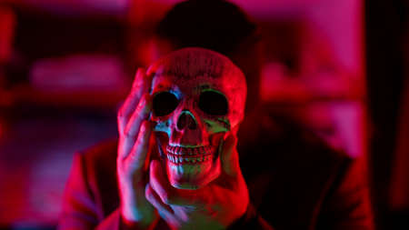 serial killer and maniac with human skull in hands, gloomy man with black mask on head