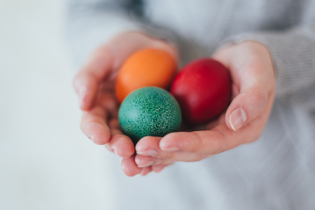 Hands holding modern easter eggs painted in red green blue. Toned pictureの写真素材