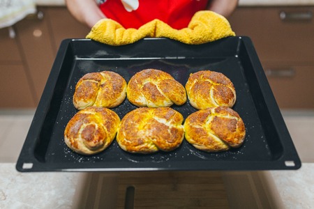 Baker hands with potholder next to metal cookie sheet with bread in ovenの写真素材