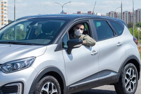 Protect yourself from the coronavirus with a mask while driving. A masked driver in a silver car