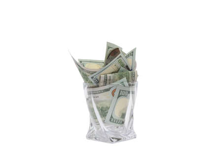 A pile of dollars stacked in a whiskey glass on a white isolated background