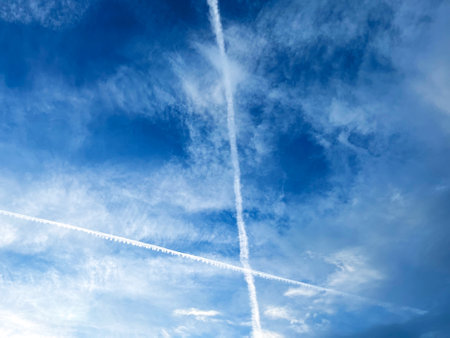 Condensation traces left by airplanes against the background of a blue cloudy sky. Intersecting white linesの写真素材