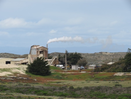 Smoke drifts from a rustic sand mine kiln building that is located amidst sand dunes that support vegetation of various shades of red and green  Taken near Marina State Beach, Calif のeditorial素材