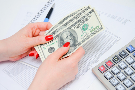 Writing of the report on work, leading of financial results. Calculation of the income. Woman hold money in hand.の写真素材