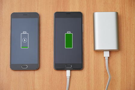 Two smart phone with charger power bank on wood table. Discharged and charged mobile. Mobile phone charger with power bank.の写真素材