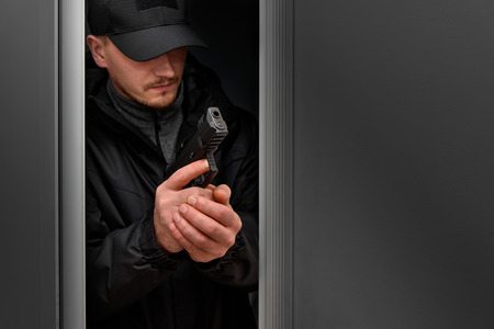 Man with the gun in dark clothes. Preparation for storm of the room. Robbery crime.