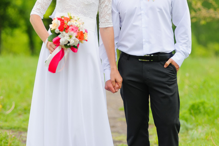 The bride holds by the groom's hand. Wedding couple holding hands. Wedding day. Warm summer day.の写真素材