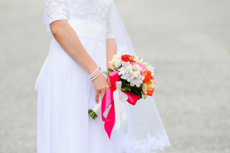 The bride gently keeps a wedding bouquet in a white dress. Romantic bride holds a beautiful wedding bouquet. Summer seasonの写真素材