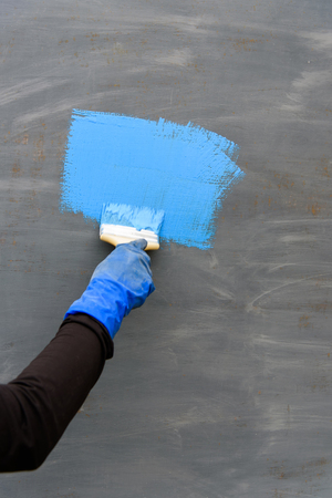 Man's hand holding paintbrush paint blue color on gray metal surface garage. Outdoor painting work. Blank paint blue color with copy spase.の写真素材