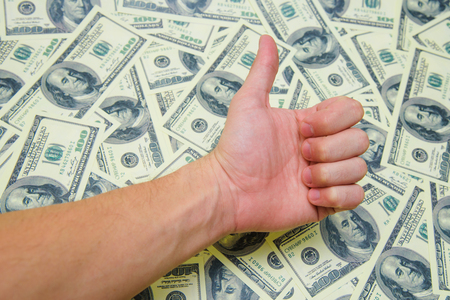 The man's hand character thumbs up against the background of money.の写真素材