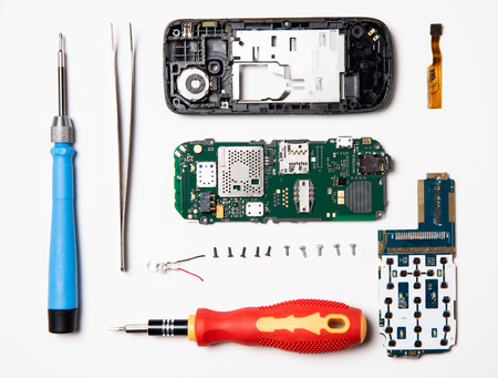 Parts of the disassembled mobile phone, screwdriver, plastic case, broken screen and parts lay out flat lay.  Service center for mobile phone repair, overhead view.の写真素材