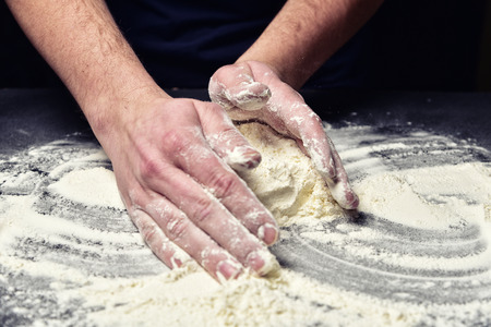 The hands of men loosen the flour for making pizza, pie. Culinary advertising close-up concept