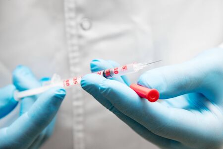 Doctor in rubber medical gloves holds a syringe with an open needle. Injection against the virus. Syringe in the hands of a doctor, close-up.の写真素材